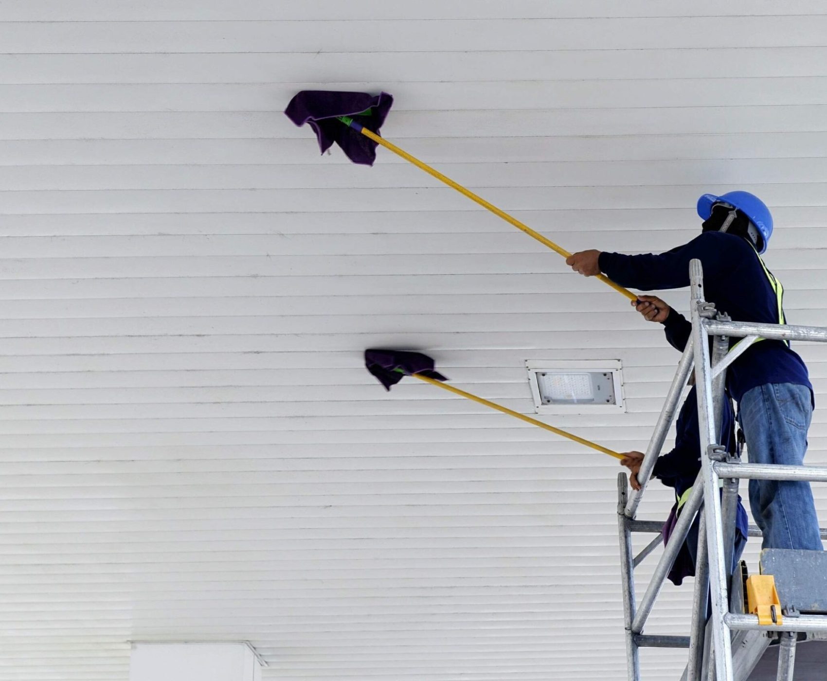 Selective focus of 2 workers on scaffolding using flat wet mops to cleaning white ceiling of petrol station, occupation concept, low angle view copy space