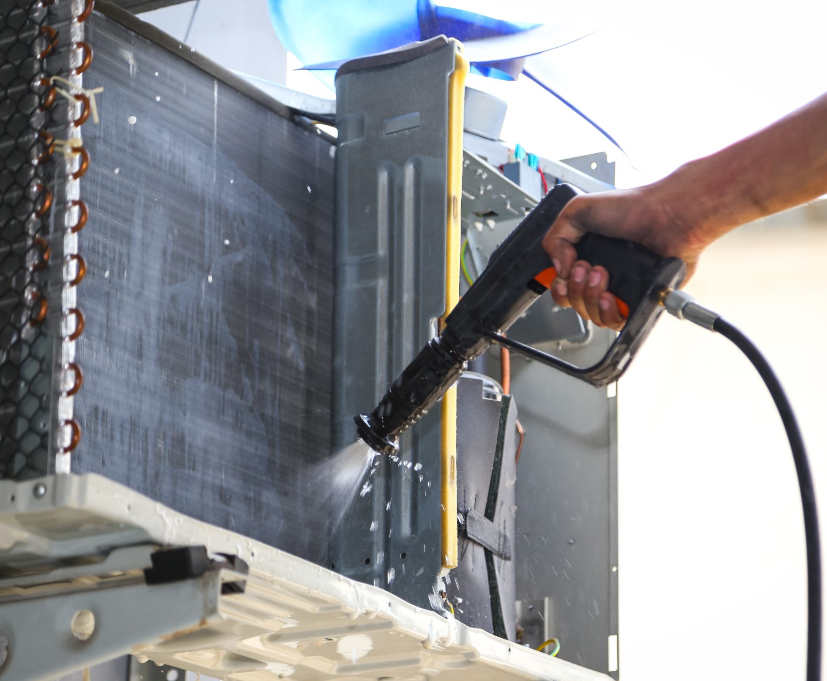 Technician cleaning air conditioner with water spray.